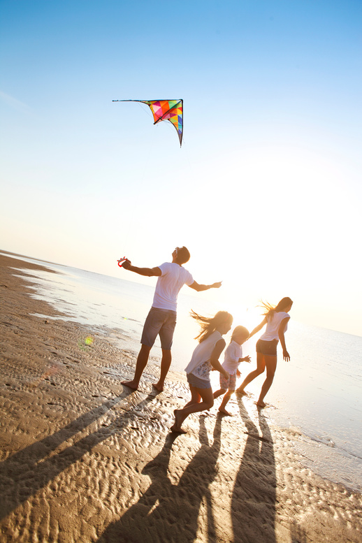 Famille jouant sur la plage avec un cerf-volant au coucher du soleil.