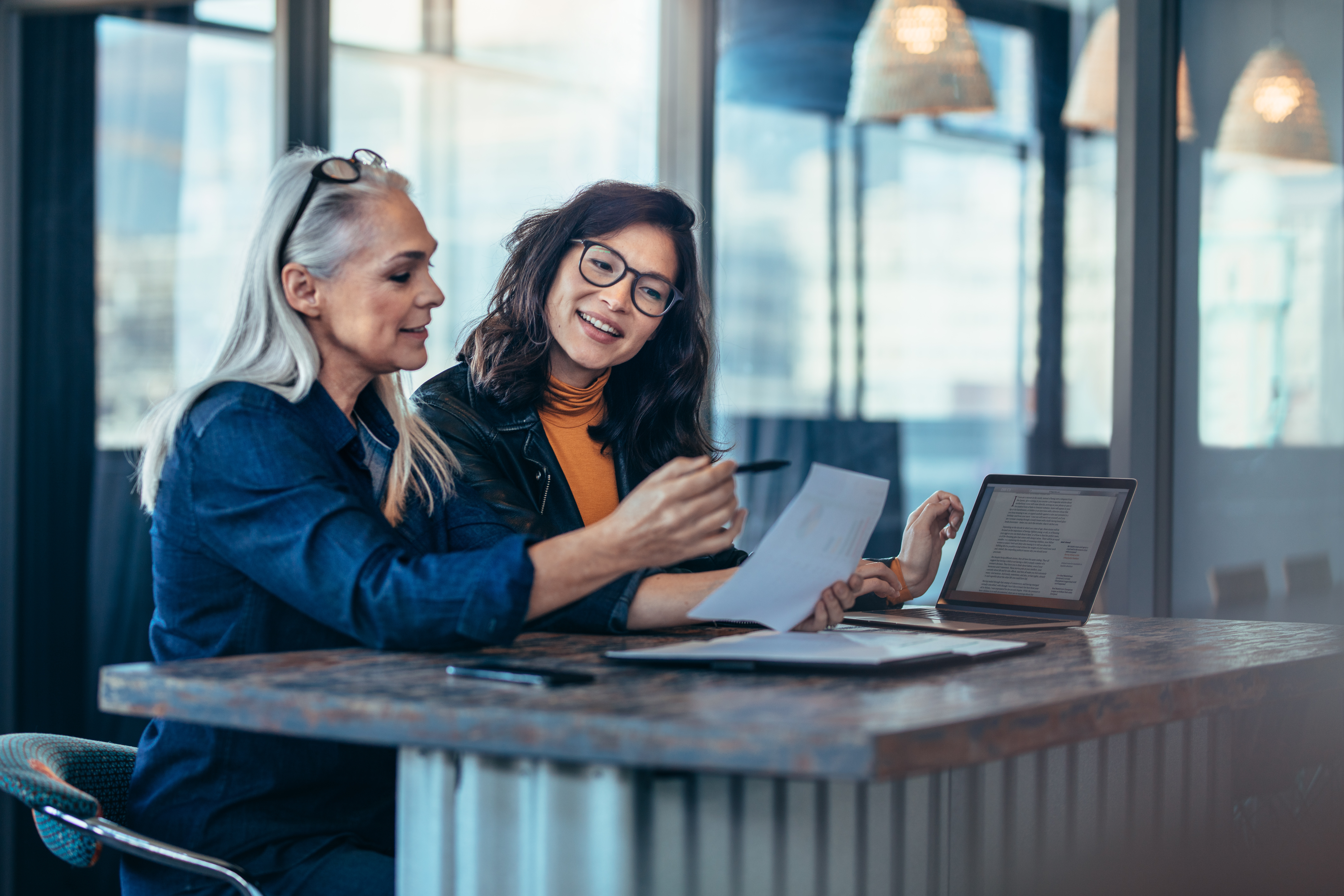 Deux femmes discutant autour d'un contrat d'assurance et d'un ordinateur portable dans un bureau moderne, illustrant le conseil personnalisé.